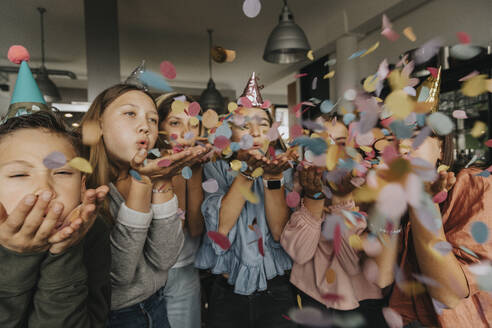 Playful friends blowing confetti while enjoying birthday party at home - MFF06132
