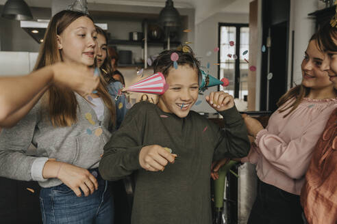 Cheerful boy wearing party hats enjoying with friends in birthday party at home - MFF06135