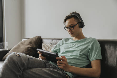 Junge Männer hören Musik und benutzen ein digitales Tablet, während sie zu Hause auf dem Sofa sitzen - MFF06144