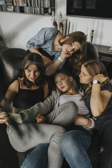 Mädchen nimmt Selfie mit Freunden beim Entspannen auf Sofa zu Hause - MFF06153
