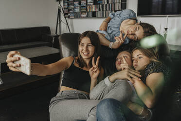 Friends gesturing while taking selfie on sofa at home - MFF06154