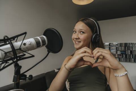 Smiling teenage girl making heart shape while singing in recording studio stock photo
