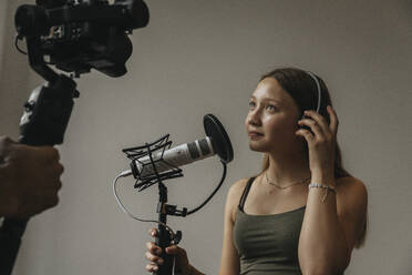 Teenager-Mädchen schaut in die Kamera, während sie über ein Mikrofon an der Wand im Studio singt - MFF06176