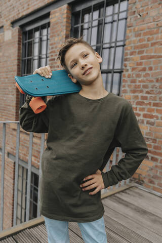 Thoughtful boy posing with blue skateboard while standing against building stock photo
