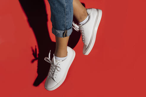 Close-up of of female wearing sneakers while jumping against red background - BOYF01430