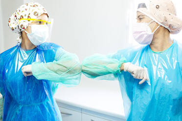 Doctor and assistant in protective workwear avoiding handshakes while greeting at clinic - JCMF01266