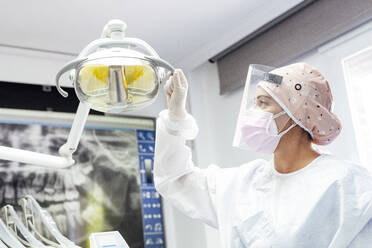 Doctor in protective workwear adjusting electric lamp in clinic - JCMF01273