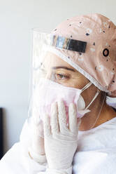 Doctor in protective suit adjusting face mask at office - JCMF01279