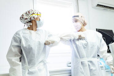 Dentist and assistant in protective workwear avoiding handshakes while standing at clinic - JCMF01282