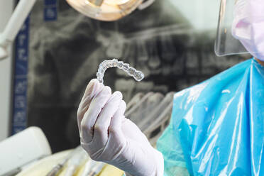 Zahnarzt mit Schutzanzug hält Zahnspange in der Hand in einer Klinik - JCMF01294