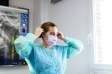 Zahnarzt im Schutzanzug mit Gesichtsmaske in der Klinik stehend - JCMF01296