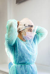Arzt im Schutzanzug mit Gesichtsschutz, während er in einer Klinik steht - JCMF01298