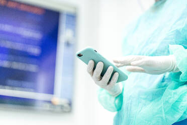 Zahnarzt im Schutzanzug, der ein Mobiltelefon benutzt, während er in der Klinik steht - JCMF01302