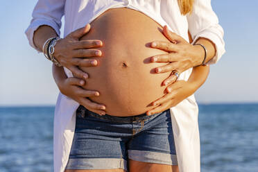 Midsection der schwangeren Frau mit Sohn berühren Bauch am Strand - DLTSF01137