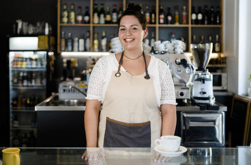 Lächelnde Besitzerin mit Kaffee auf dem Tresen eines Cafés - GIOF08759