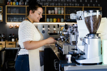 Smiling female barista making coffee through machine in cafe - GIOF08761