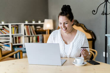 Happy voluptuous young woman doing online shopping over laptop in coffee shop - GIOF08775