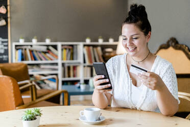 Lächelnde Frau mit Kaffee auf dem Tisch beim Online-Shopping mit dem Handy im Café - GIOF08777