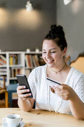 Lächelnde üppige Frau beim Online-Shopping über Handy in einem Café - GIOF08778