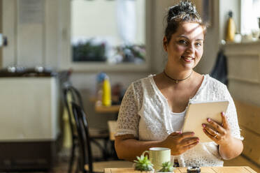 Lächelnde üppige Frau, die ein digitales Tablet benutzt, während sie in einem Café sitzt - GIOF08795