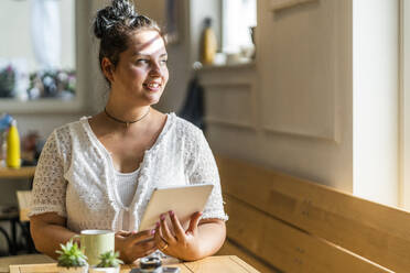 Nachdenkliche junge Frau mit digitalem Tablet, die an einem Tisch in einem Café sitzt - GIOF08796