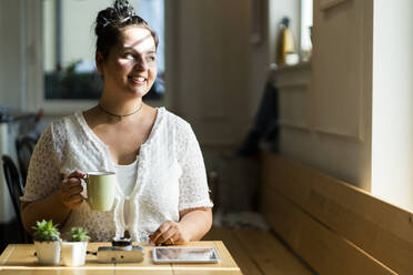 Young woman holding coffee mug contemplating while sitting at table in cafe - GIOF08797