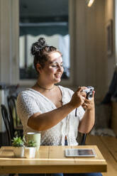 Lächelnde junge Frau, die über die Kamera in einem Café fotografiert - GIOF08799