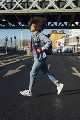 Cheerful young woman with afro hair running on street in city during sunny day - BOYF01459