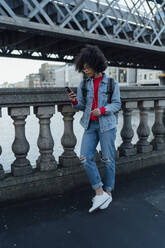 Afro young woman using mobile phone while standing on bridge in city - BOYF01464