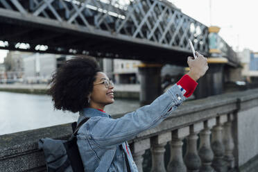 Afro junge Frau, die ein Selfie mit ihrem Smartphone macht, während sie an einem Geländer in der Stadt steht - BOYF01466