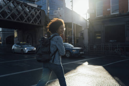 Afro young woman with backpack crossing street in city - BOYF01467