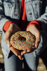 Nahaufnahme einer jungen Frau mit Jeansjacke, die einen Donut hält - BOYF01470