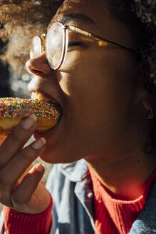 Nahaufnahme einer jungen Frau mit Brille, die einen Donut isst - BOYF01477