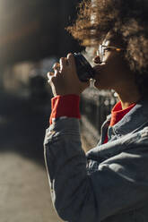 Nahaufnahme einer jungen Frau mit Afrolook, die an einem sonnigen Tag Kaffee trinkt - BOYF01479