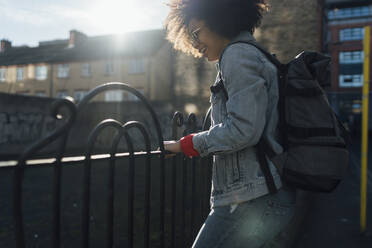 Unbekümmerte junge Frau mit Rucksack an einem Geländer in der Stadt an einem sonnigen Tag - BOYF01482