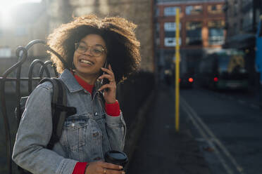 Afro junge Frau spricht über Handy, während sie auf der Straße in der Stadt steht - BOYF01485