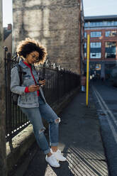 Afro young woman using mobile phone while standing by railing on street in city - BOYF01488