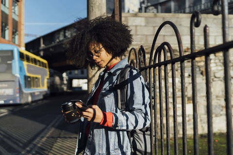 Young woman with curly hair using smart phone while standing by railing in city stock photo