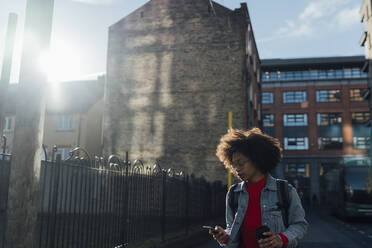 Afro young woman using smart phone while standing against buildings in city - BOYF01493