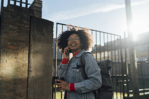 Afro woman talking over mobile phone while standing against sky during sunny day stock photo