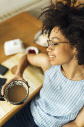 Nahaufnahme einer jungen Frau mit geschlossenen Augen, die eine Kaffeetasse hält, während sie am Tisch sitzt - BOYF01504
