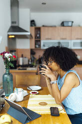 Businesswoman with curly hair drinking coffee while sitting at desk in home office - BOYF01505