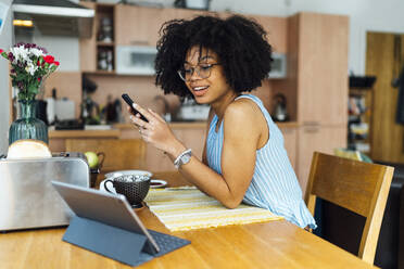 Unternehmerin mit lockigem Haar, die ihr Smartphone am Schreibtisch im Home Office benutzt - BOYF01506