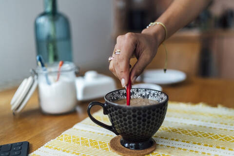 Nahaufnahme einer jungen Frau, die mit der Hand Kaffee in einer Tasse auf einem Tisch zu Hause mischt, lizenzfreies Stockfoto
