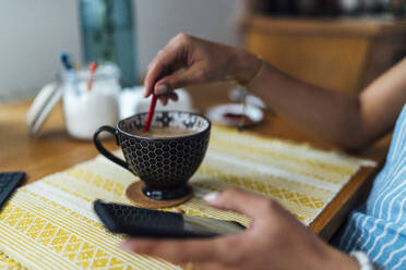 Close-up of businesswoman with coffee cup on desk using smart phone at home - BOYF01514