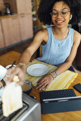 Junge Frau mit digitalem Tablet auf dem Tisch macht Frühstück zu Hause - BOYF01517