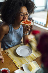 Junge Frau mit geschlossenen Augen, die am Tisch sitzend Brot isst - BOYF01521