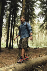Mittlerer erwachsener Mann, der auf einem Baumstamm gegen Bäume im Wald läuft - BOYF01532