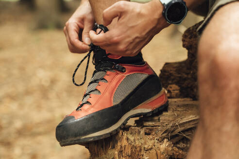 Close-up of mid adult man tying shoelace on wood in forest - BOYF01541