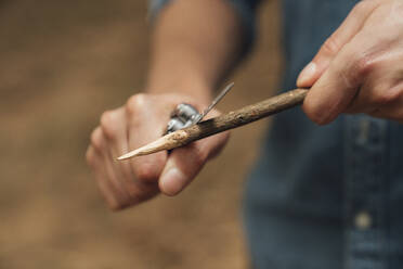 Nahaufnahme eines erwachsenen Mannes, der mit einem Taschenmesser im Wald Holz schneidet - BOYF01543